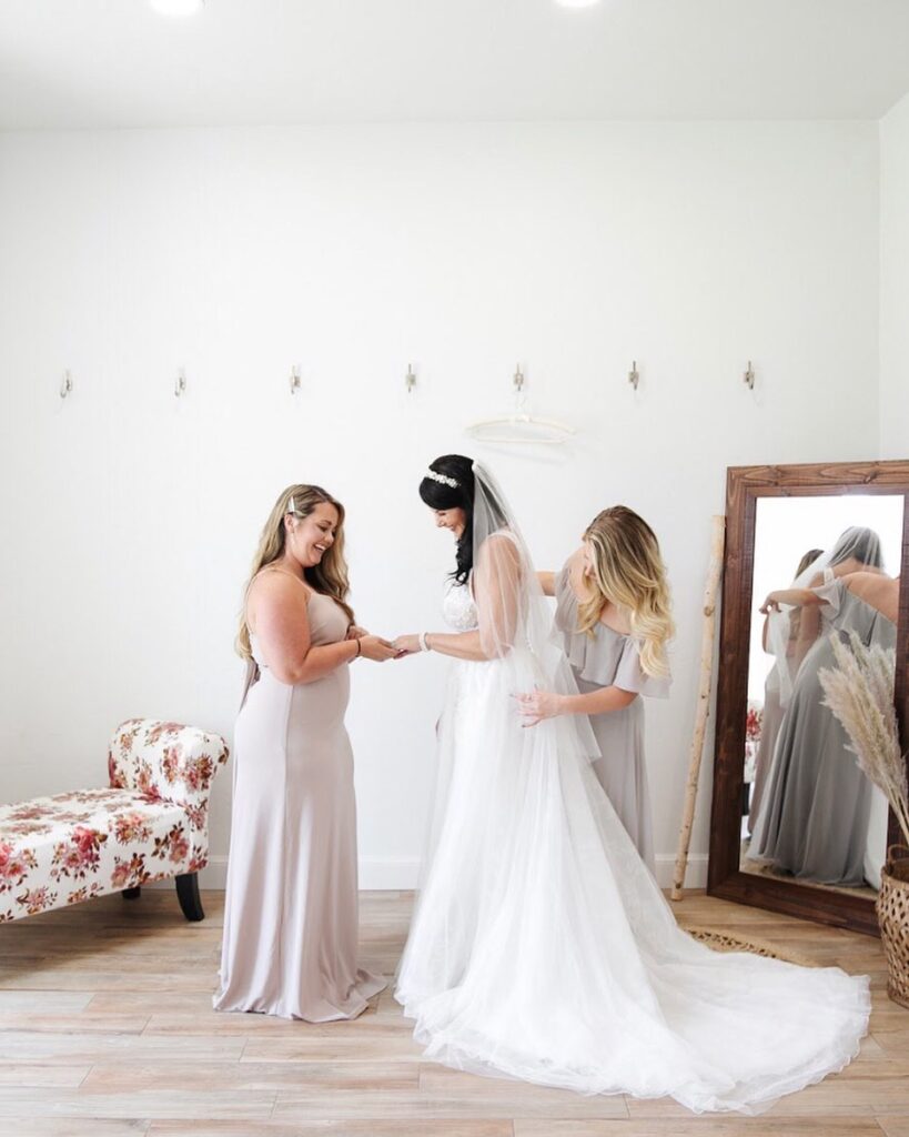 bridesmaids helping bride put on dress