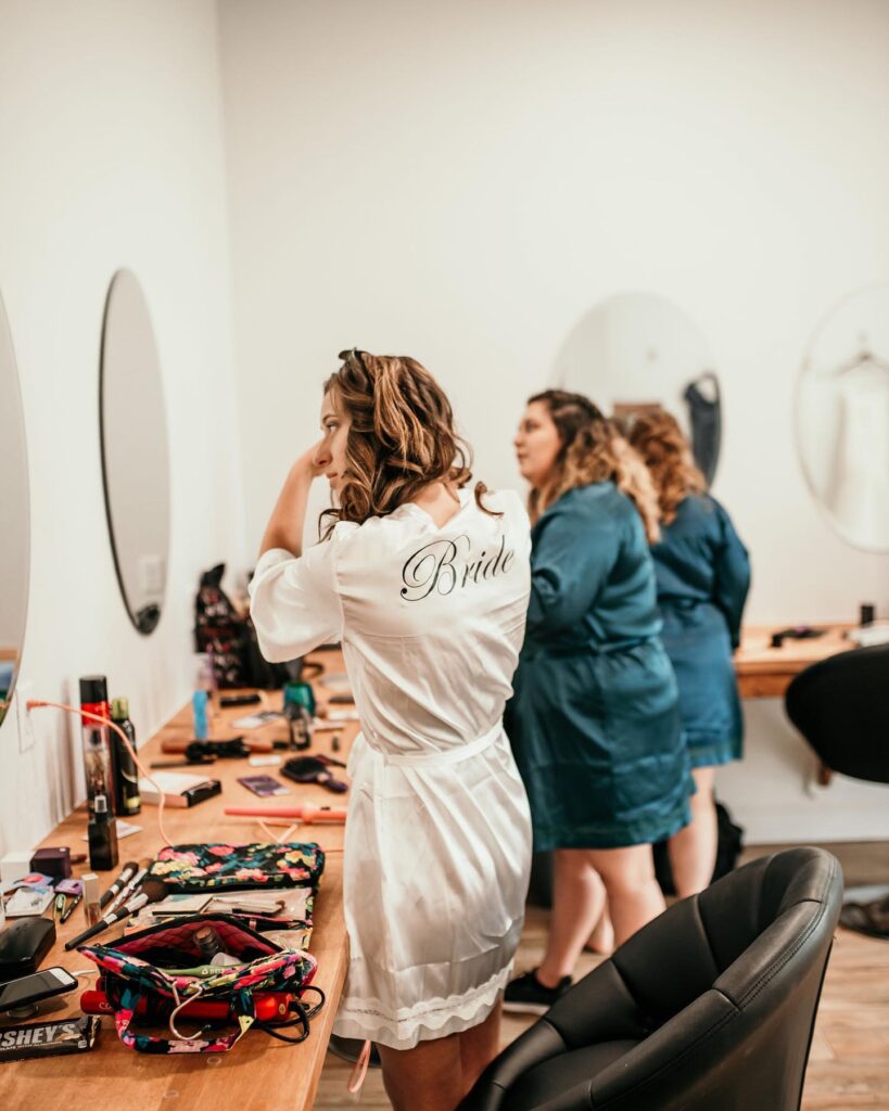 bride and bridesmaids putting on makeup and styling hair